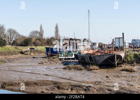 Fiume Roach a bassa marea vicino a Rochford e Stambridge, Essex, Regno Unito. Navi vecchie e in decadimento. Barche che si siedono sul fango vicino al cantiere Foto Stock