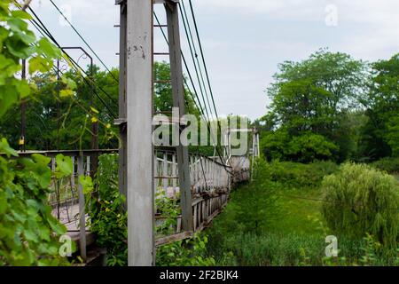 Vecchio ponte sospeso in ferro non funzionante su una vista laterale del fiume essiccato. Foto Stock