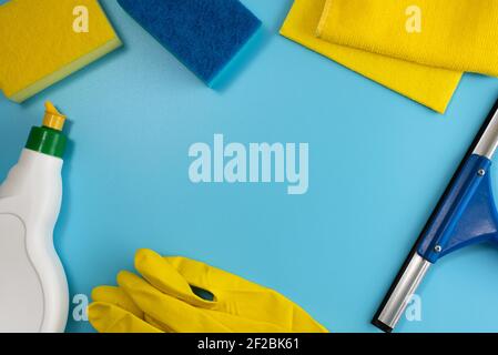 Vista dall'alto dei prodotti per la pulizia della casa: Guanti in gomma, spugne, panni, spatola e detergente su sfondo blu. Spazio di copia. Disposizione piatta Foto Stock