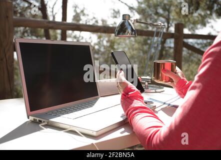 donna con telefono in mano, tavolo da lavoro con influencer esterno con computer, e forniture per ufficio, Foto Stock