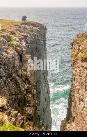 Birdwatcher seduto in cima alle scogliere di mare a Brough of Birsay, Orkney. Foto Stock