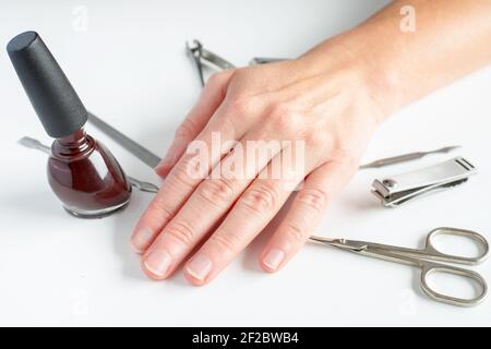 Attrezzi per manicure e mano femminile su sfondo bianco. Fare self-manicure a casa concetto. Foto Stock