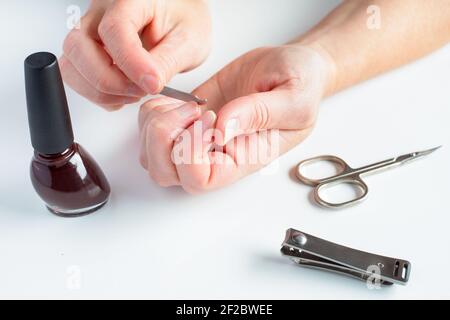 Le mani della donna fanno manicure. Mani femminili, lima per unghie, con smalto per unghie, forbici e tagliaunghie su sfondo bianco. Foto Stock