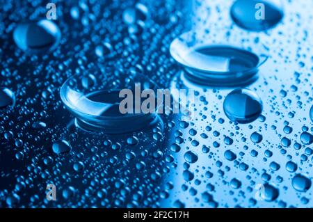 Primo piano di due lenti a contatto con gocce su sfondo scuro. Immagine con tonalità blu. Foto Stock