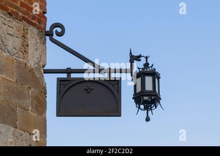 Cartello nero in metallo vecchio stile con lanterna appesa l'angolo di un muro di pietra Foto Stock