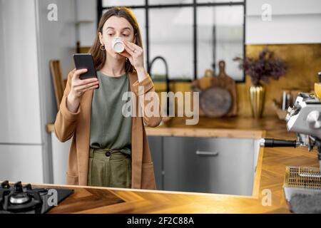 Giovane donna irritata che ha fretta di lavorare al mattino, indossa una giacca, beve caffè e chiacchiera al telefono mentre sei in viaggio. Routine quotidiana di donna d'affari. Foto Stock