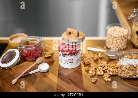 Sana colazione con muesli in vaso di vetro con lampone e yogurt biologico su tavolo in legno in cucina con noci sullo sfondo. Spazio di copia Foto Stock