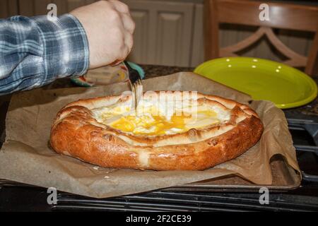 Khachapuri georgiano - fresco dal forno con burro di fusione in formaggio caldo e mescolando a mano nel burro e. uova crude Foto Stock