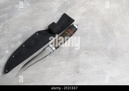 Un elegante coltello da caccia con scabarda e manico in pelle su fondo grigio cemento. Messa a fuoco selettiva. Foto Stock
