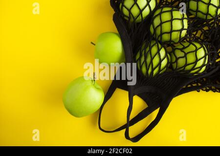 Nessun concetto di sacchetto di plastica. Borsa nera di shopping in mesh con mele verdi su sfondo giallo. Vista dall'alto. Spazio di copia. Foto Stock