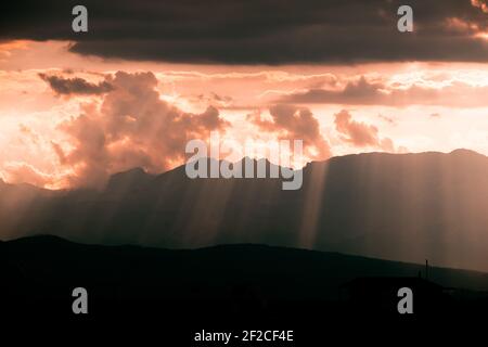 Una vista mozzafiato di un sole che si infrangono attraverso nuvole e silhouette di montagna alayered Foto Stock