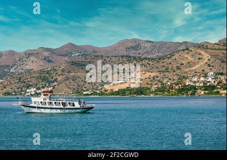 Creta, Grecia - una piccola nave a vela bianca nel mediterraneo vicino Elounda contro montagne rocciose e cielo blu Foto Stock