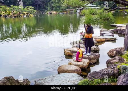 03/23/2015 Tokyo Giappone Madre e figlio che guardano su carpe KOI. Bel giardino con stagno artificiale KIYOSUMI TEIEN giardino. Arriva la primavera. Foto Stock