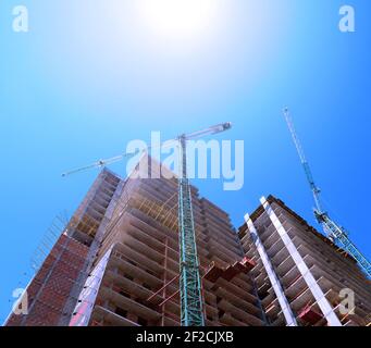 Un sole bianco splende su una gru di costruzione e su una casa incompiuta. Casa a più piani in città Foto Stock
