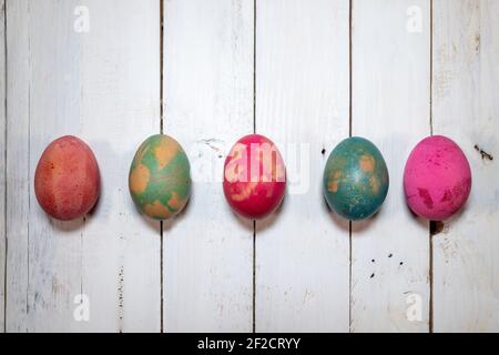 Un modo naturale fatto in casa per decorare le uova di Pasqua. Cinque uova bollite dipinte con colori, foglie e fiori su un elegante tavolo in legno shabby. Foto Stock