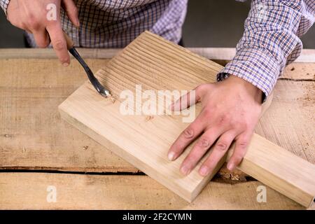 Le mani del falegname sul lavoro fanno scanalature sul tagliere di legno superficie con closeup scalpello Foto Stock