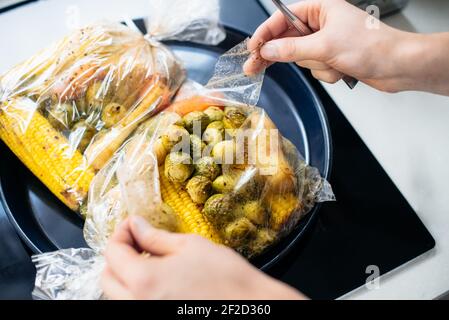 Piatto da forno a base di piante di apertura a mani maschili con germogli di bruxelles, radice di prezzemolo, mais. Mescolare le verdure in un sacchetto da forno sul vassoio. Cuocere le verdure sane Foto Stock
