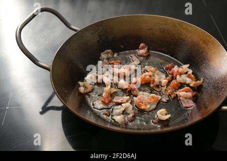 Pezzi croccanti tritati di pancetta fritti in una padella di ferro sulla stufa nera, spazio di copia, fuoco selezionato, profondità di campo stretta Foto Stock