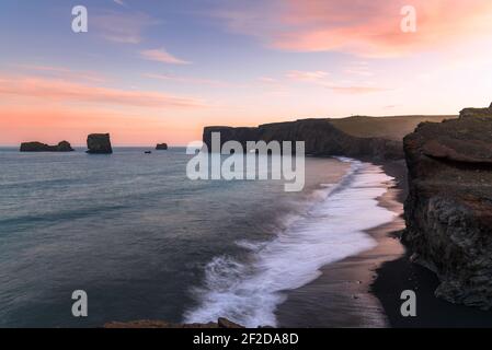 Promontorio roccioso che si affaccia su una baia e una spiaggia di sabbia nera sotto un bel cielo illuminato dal sole di mezzanotte in estate Foto Stock