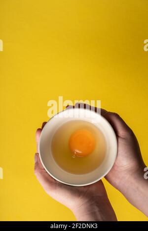 Vista dall'alto uova biologiche fresche in mani che tengono sopra il giallo sfondo Foto Stock