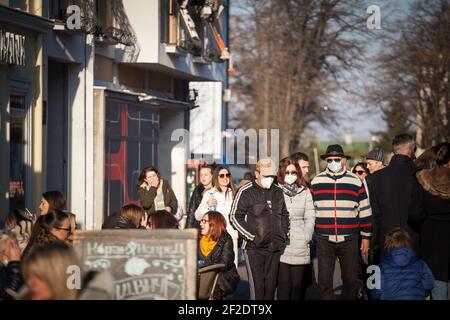 BELGRADO, SERBIA - 21 FEBBRAIO 2021: Persone, uomini e donne, giovani e anziani, alcuni indossano una maschera facciale in una strada affollata con persone che siedono nei caffè Foto Stock