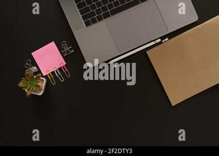 Scrivania da lavoro con computer portatile e carta per appunti su sfondo nero, inclusa un'area di copia per aggiungere testo o grafica. Foto Stock