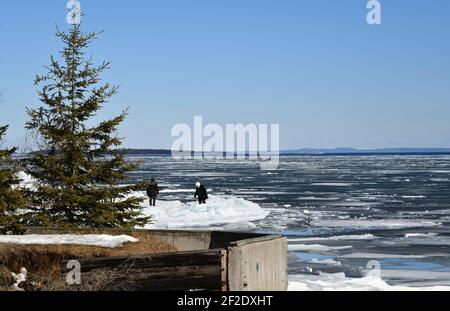 Due persone in lontananza sulla riva del lago superiore durante la pausa primaverile in una giornata di sole. Foto Stock