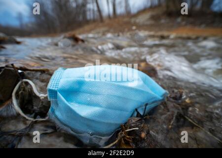 Maschera facciale scartata, maschera COVID gettata in un torrente in un parco pubblico Foto Stock