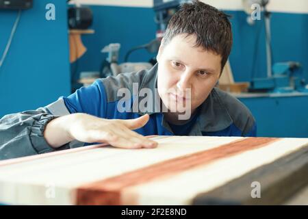 Un cabinettista lavora con legno in un negozio di carpenteria. Un giovane lavoratore di aspetto caucasico fa un piano di lavoro. Foto Stock