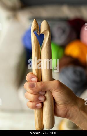 Due aghi in legno per maglieria in una mano femminile sul sfondo di matasse di merino multicolore a forma di a. cuore Foto Stock