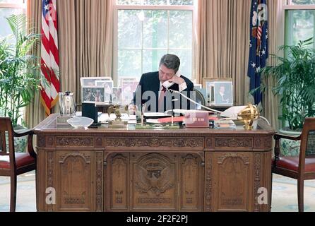 Il presidente Ronald Reagan durante una telefonata al membro del Congresso per aver fatto pressione sulla sua scrivania nell'ufficio ovale. Foto Stock