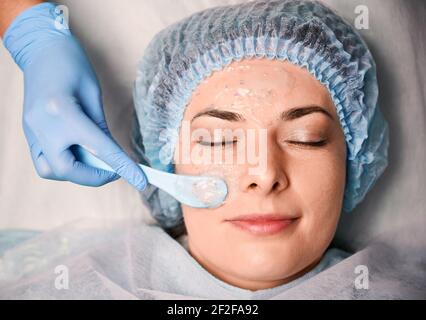 Mano cosmetologa che applica la maschera cosmetica sul viso della donna. Foto Stock