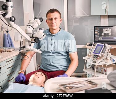 Giovane dentista maschile seduto al posto letto paziente in studio dentale. Foto Stock