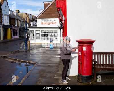 Un uomo anziano in un cappello piano che postava una lettera nel centro di Whitstable. Foto Stock