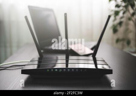 Router WI-FI connesso a Internet sul tavolo e sul computer portatile sullo sfondo Foto Stock