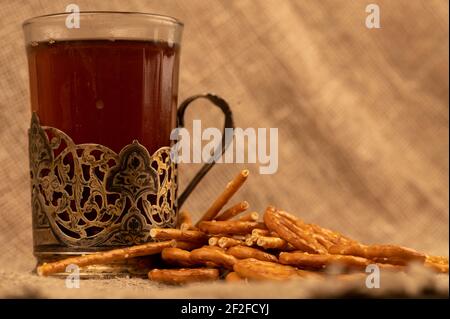 Grissini salati e pretzel salati sfusi e un bicchiere di tè in un portabicchieri sul tavolo. Messa a fuoco selettiva in primo piano. Foto Stock