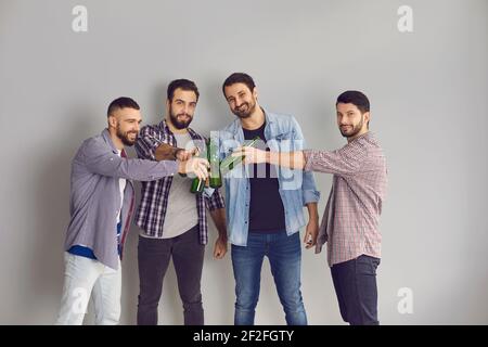Gruppo di uomini che si aggraffano le bottiglie di birra e guardano la macchina fotografica in studio con sfondo grigio Foto Stock