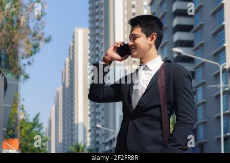 Un uomo d'affari asiatico sta parlando con il suo collega al telefono per le strade della città durante il tuo viaggio mattutino. Foto Stock