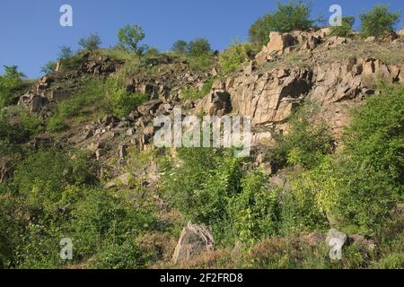 Un pendio roccioso di una cava di granito abbandonata nella regione di Nikolaev in Ucraina in una calda giornata estiva. Pietre affilate sopravite con vegetazione sparsa. Blu Foto Stock