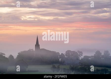 Il campanile della chiesa di St Barnaba a Weeton, Lower Wharfedale, è visibile sopra una coperta di nebbia estiva durante un'alba color pastello ad agosto. Foto Stock