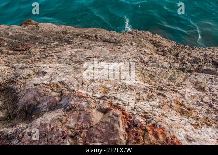 Le onde turchesi del mare si rompono sul paesaggio roccioso. Onde di mare e rocce. L'acqua di mare pura e limpida, grandi pietre da vicino. Onda morbida che schiaccia la pietra enorme a baia. Foto Stock