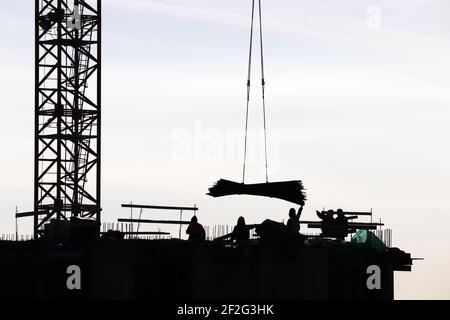 Sagome di operai e gru sul cantiere contro il cielo. Edilizia abitativa, costruttori che lavorano su ponteggi Foto Stock
