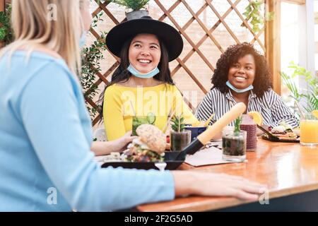 Felici amici multirazziali che mangiano al ristorante brunch durante il coronavirus Focolaio - fuoco sulla ragazza asiatica