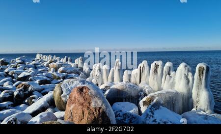 pali di legno surgelato sulla riva del mare con acqua blu e cielo blu in una giornata di sole inverno. paesaggio invernale Foto Stock