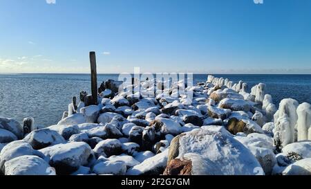 pali di legno surgelato sulla riva del mare con acqua blu e cielo blu in una giornata di sole inverno. paesaggio invernale Foto Stock