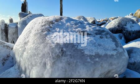 pali di legno surgelato sulla riva del mare con acqua blu e cielo blu in una giornata di sole inverno. paesaggio invernale Foto Stock