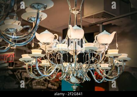 Lussuoso grande lampadario, lampade sotto forma di teiera e tazze e piattini in porcellana. Base in ferro. Foto Stock