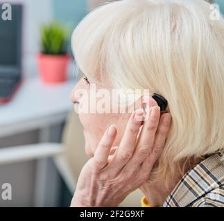 La donna anziana con apparecchio acustico dietro l'orecchio ascolta i suoni dell'ambiente. Concetto di trattamento per la perdita dell'udito nelle persone anziane Foto Stock