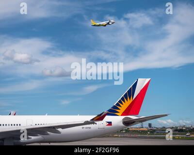 Philippine Airlines Airbus A330 al Terminal 2 dell'aeroporto internazionale Ninoy Aquino di Manila, con Cebu Pacific Airbus A320 che vola sopra. Foto Stock