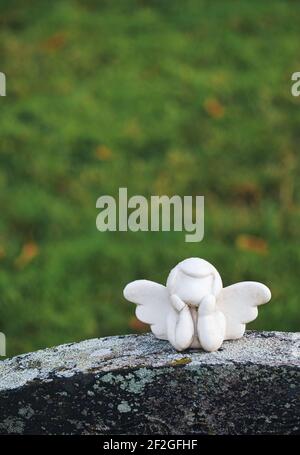 Piccola scultura d'angelo senza volto bianca alata con testa in mano sopra la lapide. Concetto di memoria, morte, spiritualità Foto Stock